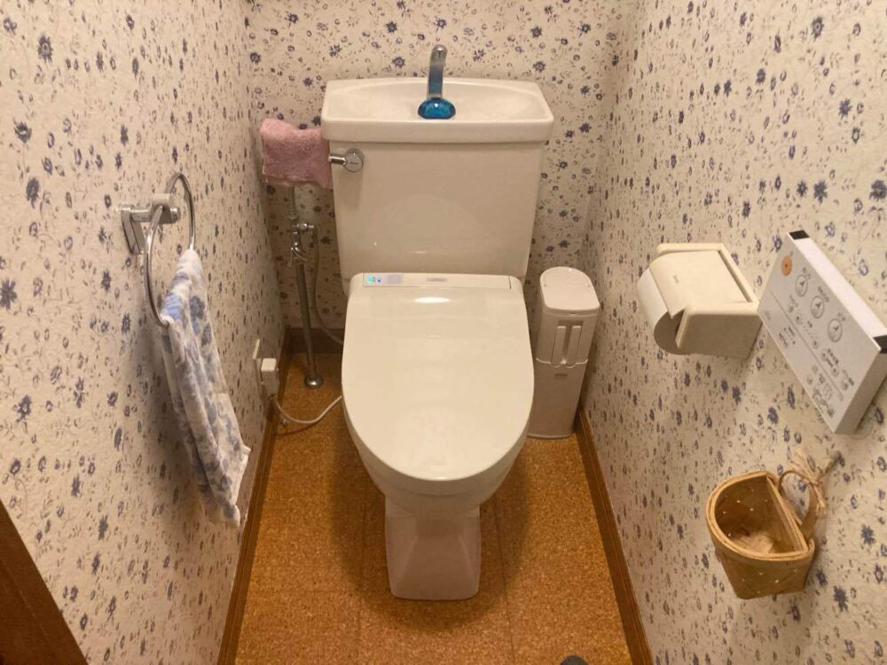 施工前：花柄のクロスとコンパクトな空間が印象的なトイレ。温かみのある内装で、長く大切に使われてきた様子がうかがえます。
